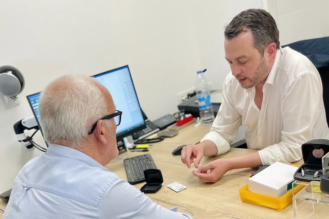 Un audioprothésiste SONARIS explique le fonctionnement d’une aide auditive à un patient en cabine